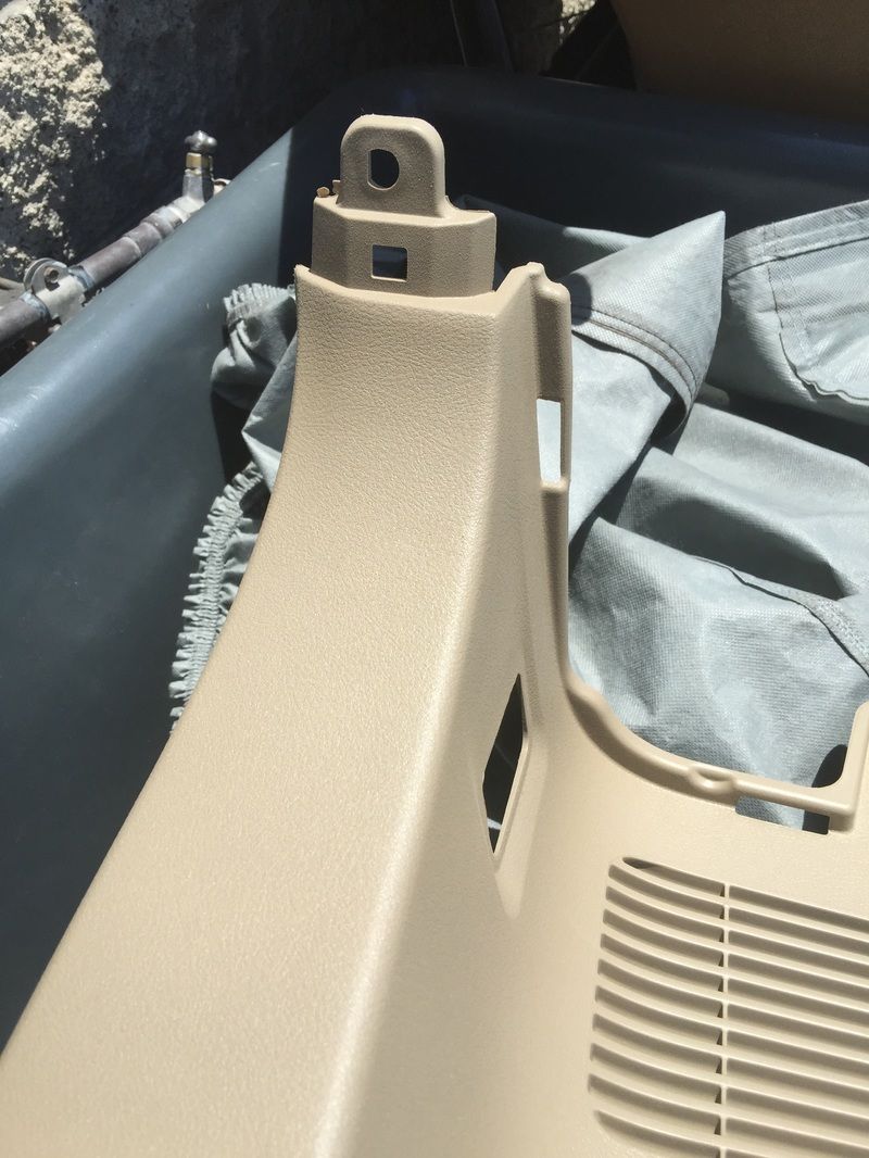 Beige plastic cargo area panel with a metal mounting bracket, beside folded gray fabric in a vehicle bed.