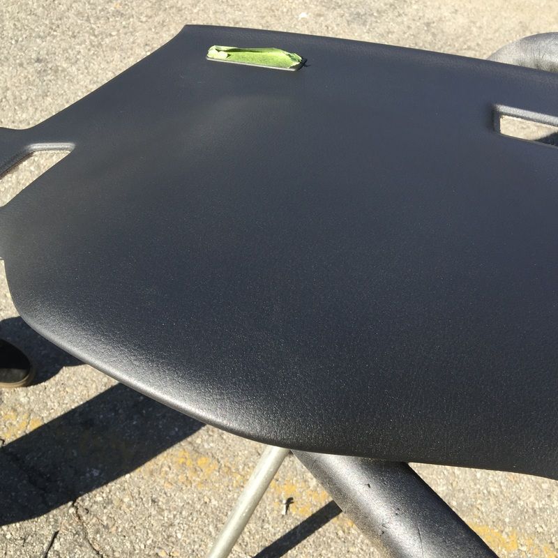 Black molded chair seat with a small green object on it, viewed outdoors on pavement.