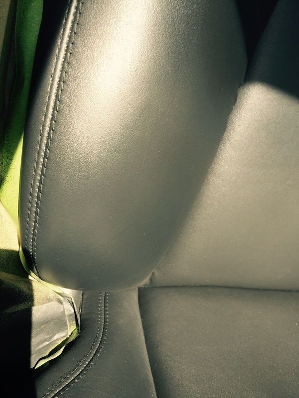 Close-up of black leather car seat with stitched seam and sunlight on the cushion