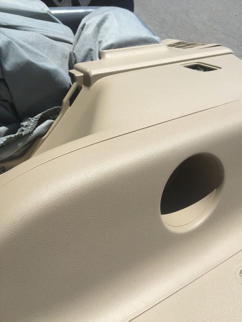 Beige car interior panel with a round cup holder opening and a blue cloth draped nearby.