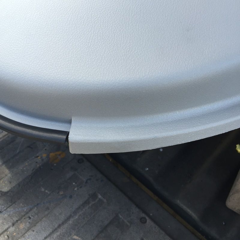 Close-up of a white vehicle bumper and trim above a black rubber floor mat.