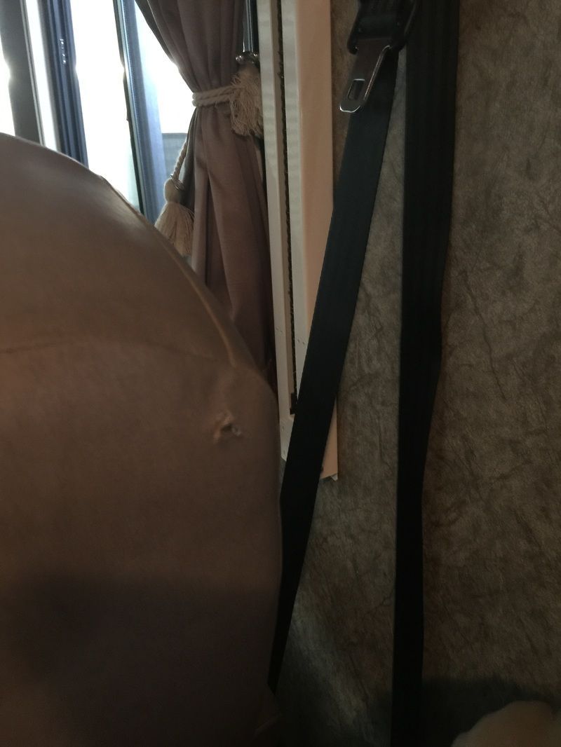 Close-up of a brown seat beside a window with curtains and a black strap hanging down