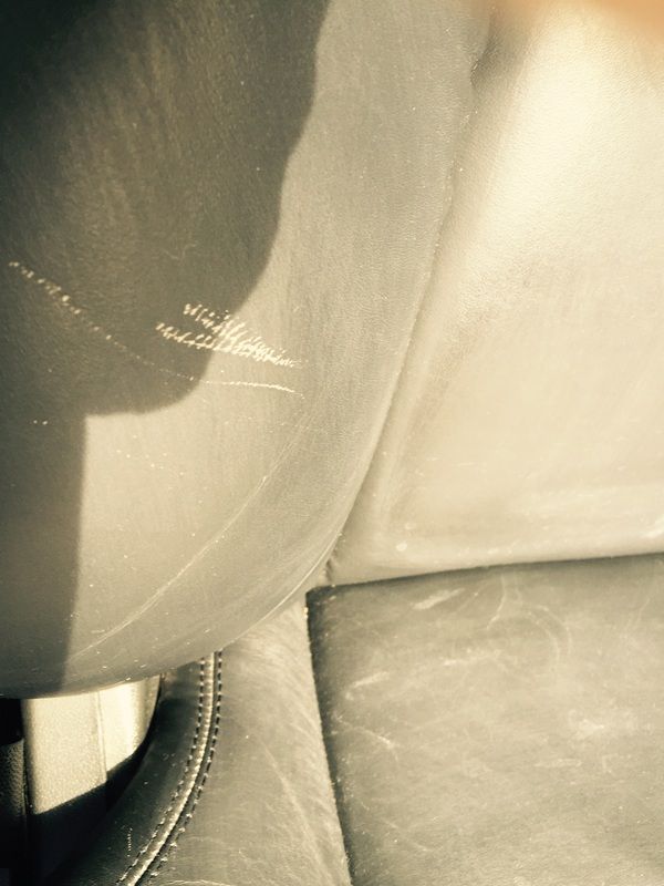Close-up of a worn leather car seat with visible stitching and sunlight glare