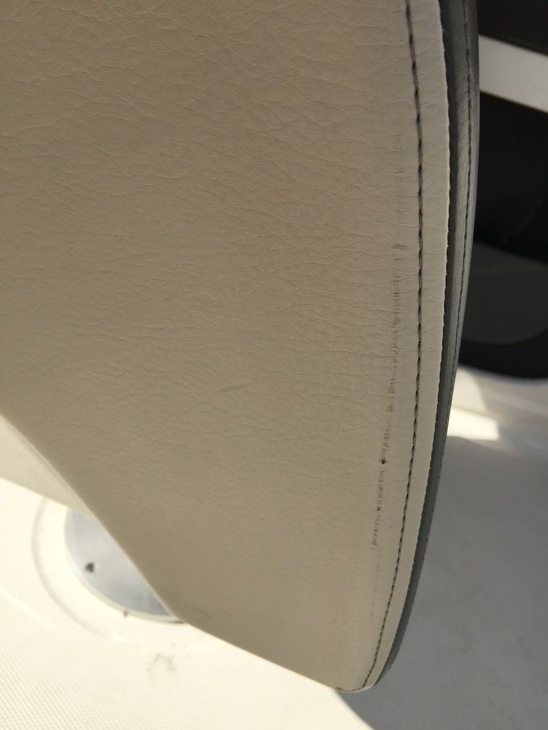 Close-up of a beige upholstered chair edge with visible stitching and a white base underneath.
