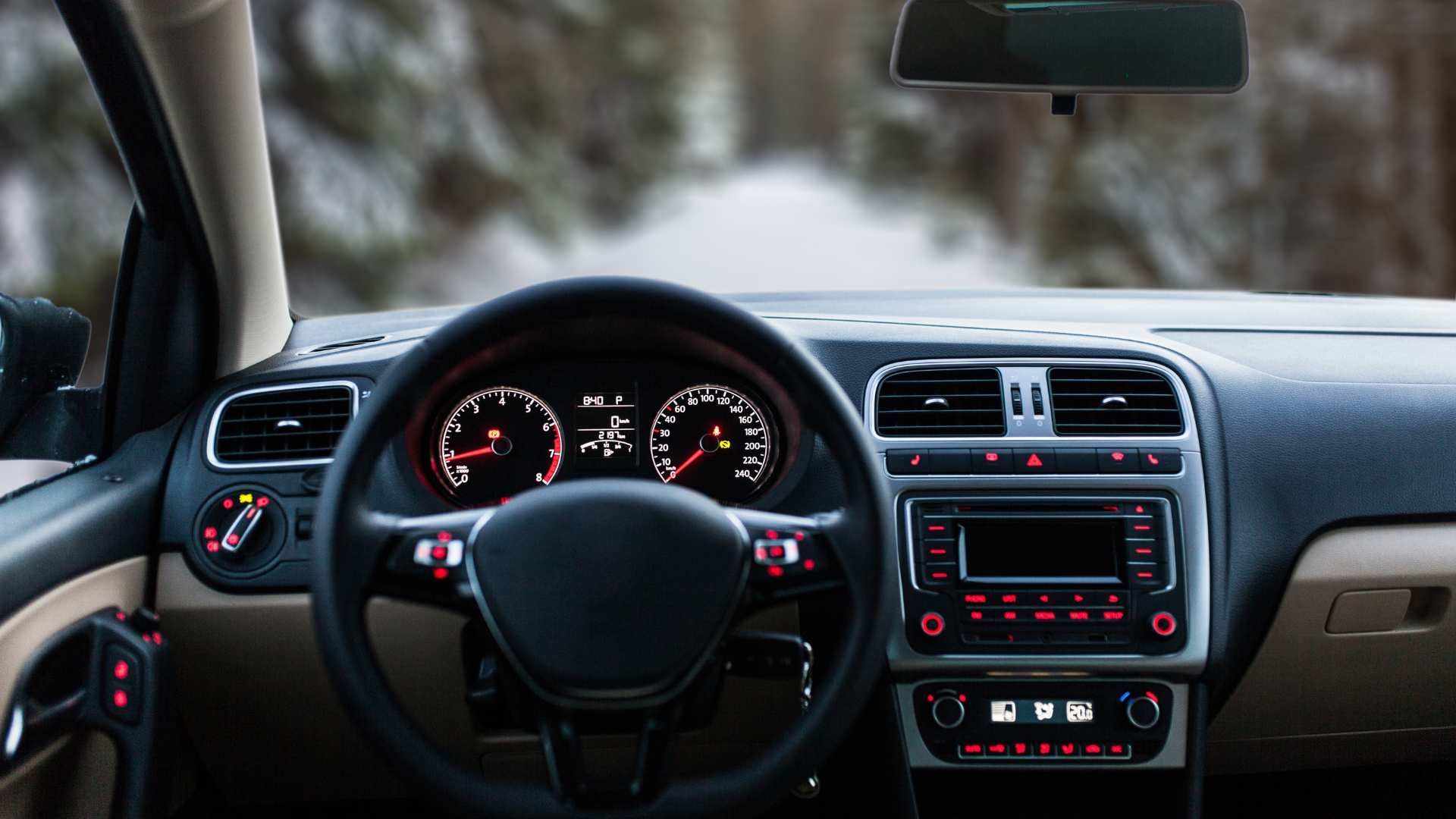 Car dashboard and steering wheel with illuminated gauges, parked in a snowy outdoor setting