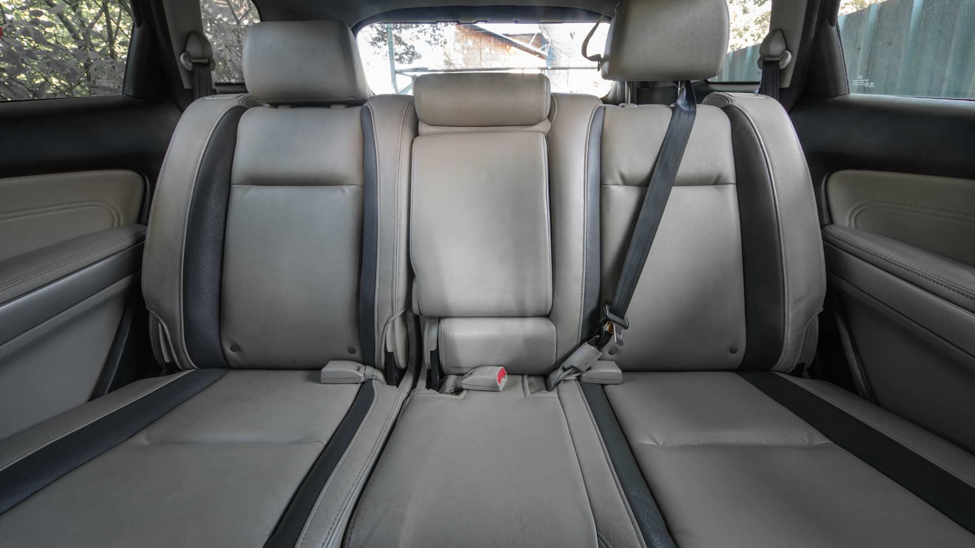 Back seat of a car with gray leather seats and seat belts visible