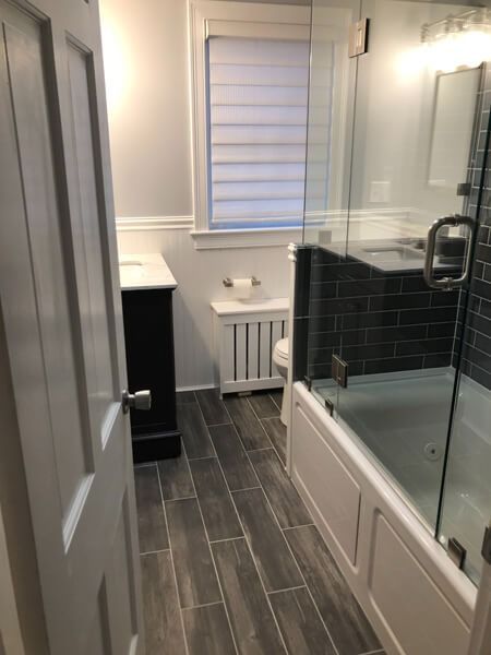 Bathroom with gray wood-look tile, white tub, black tile accent wall, and glass shower door.