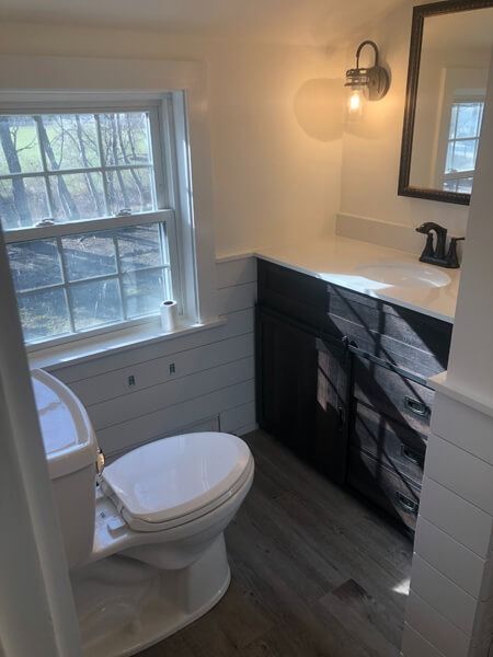 Small bathroom with toilet, vanity, window, and wood-look flooring.