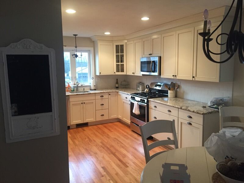 Cream-colored kitchen with wood floor, cabinets, stainless steel appliances, and a round table. A chalkboard hangs on the wall.