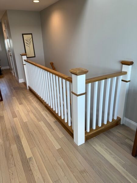 Wooden staircase with white railings, hardwood floors, and gray walls.