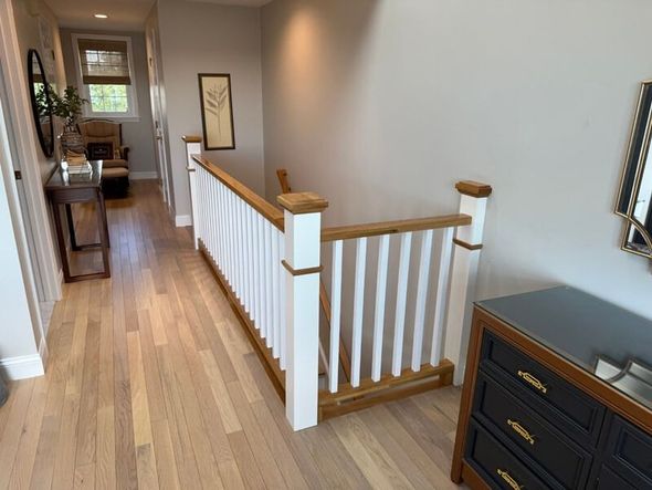 Hallway with light hardwood floors, staircase with white railing, and a dark dresser.