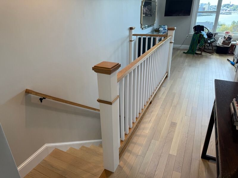 Staircase with white railing, wood handrail, leading down. Light wood floors, neutral walls, and window view.