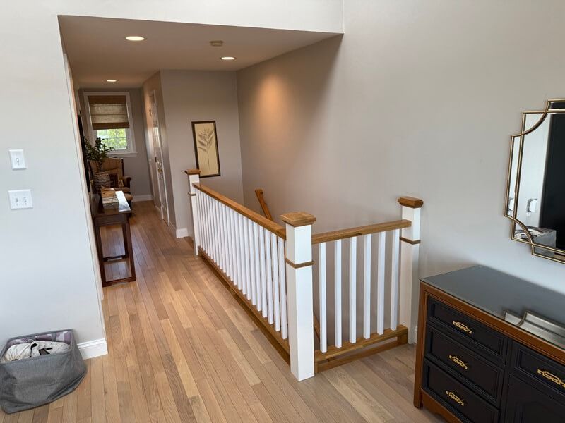 Hallway with light wood floors, a staircase with white balusters, and gray walls.
