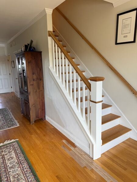 Wooden staircase with white balusters, light wood treads, and wooden handrails in a house.