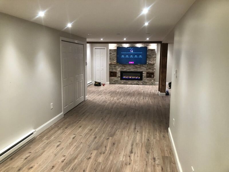 Long, narrow room with wood-look flooring, recessed lighting, and a fireplace with a TV.
