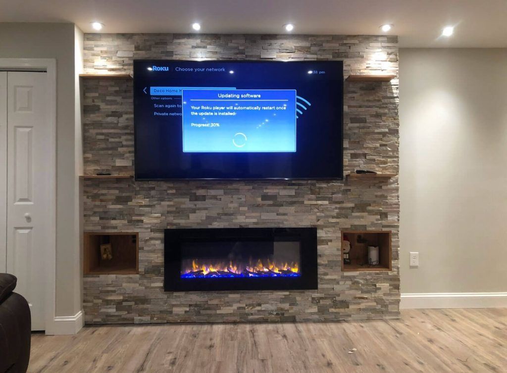 Fireplace with a mounted TV on a stone accent wall, recessed shelving, and wooden trim.