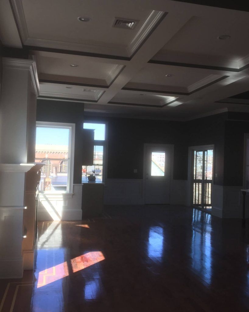 Empty room with dark walls, coffered ceiling, hardwood floor, sunlight through windows.
