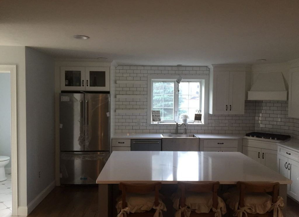 Spacious kitchen with island, stainless steel appliances, white cabinetry, and a brick backsplash.