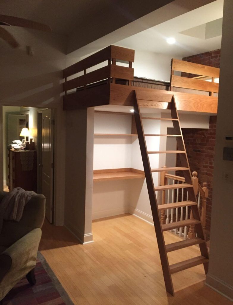 Loft bed with wooden frame and ladder over desk and shelves in a room with hardwood floors.