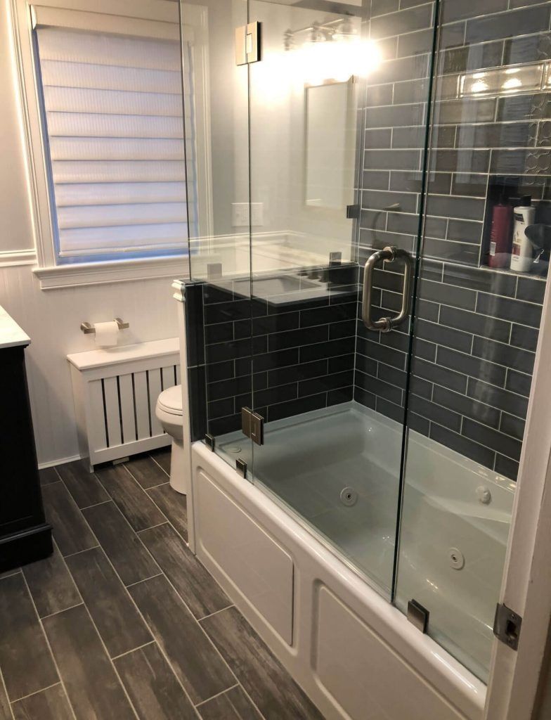 Modern bathroom with a glass shower enclosure, dark tiled walls, and white tub.