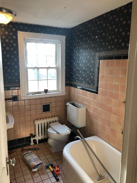 Bathroom with pink tile, wallpaper, and a white tub, toilet, and window.