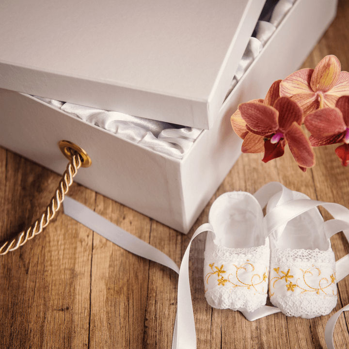 A pair of white baby shoes sitting next to a white box