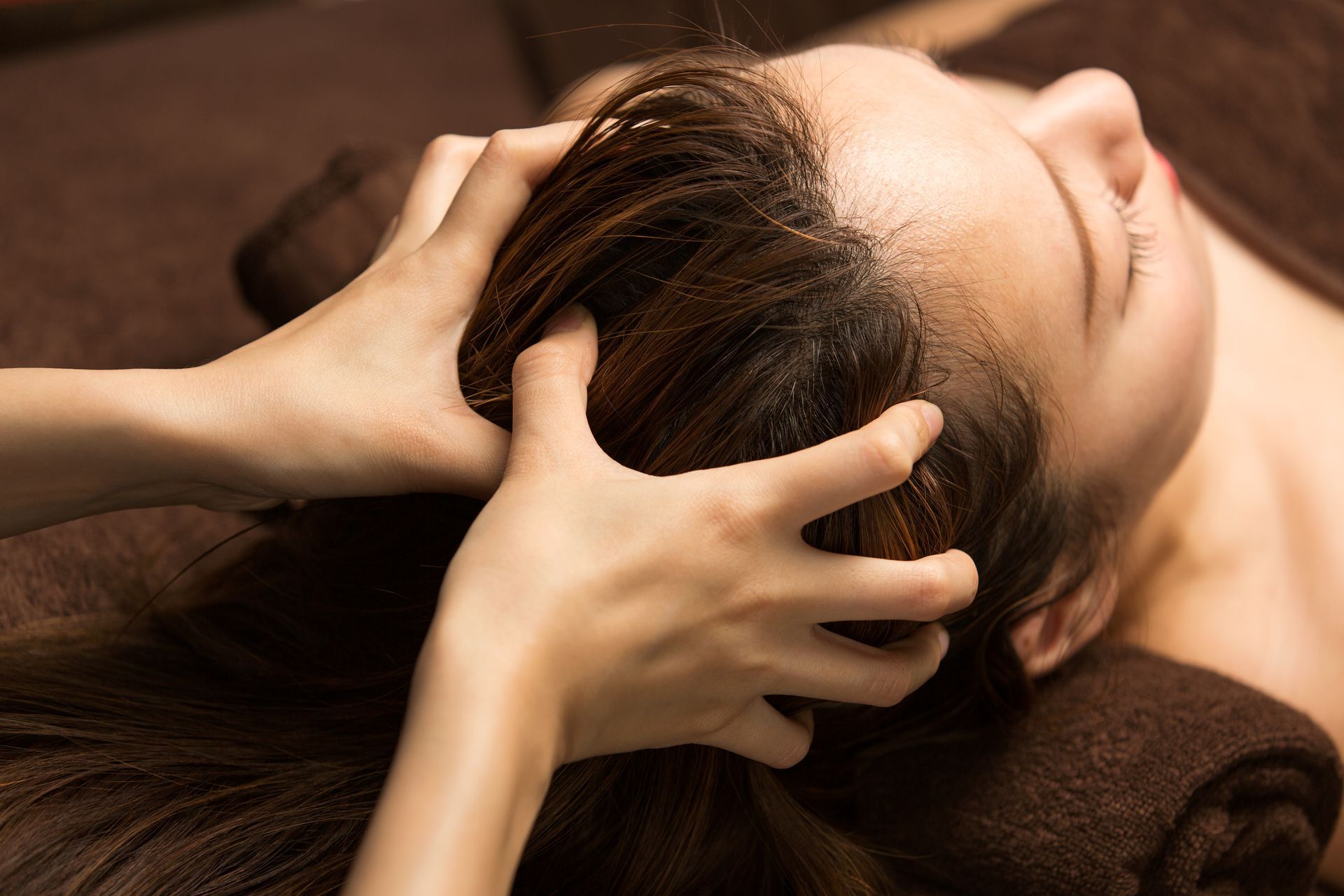 Hands massaging a person’s scalp during a head spa treatment on a brown towel.