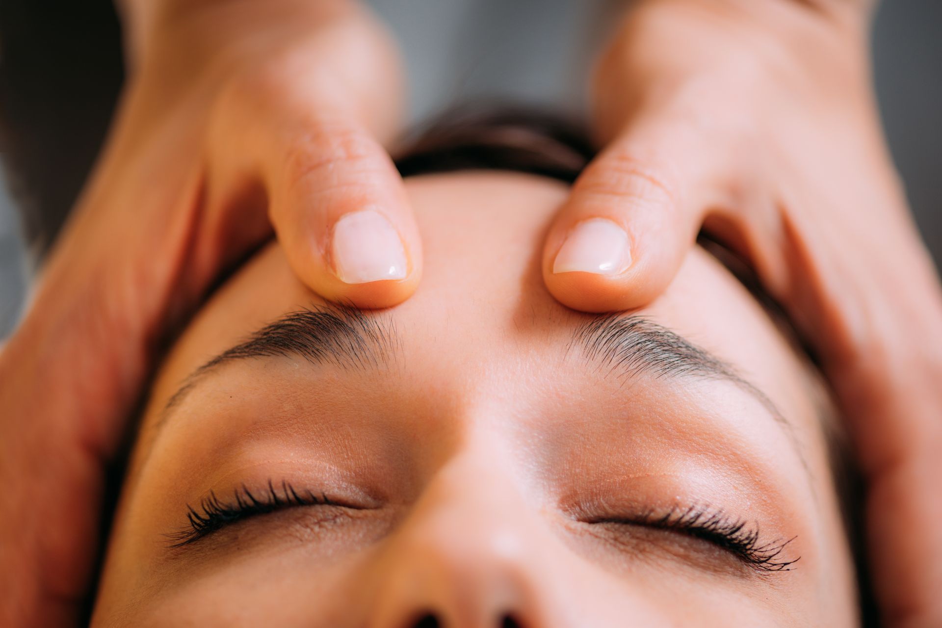 Hands gently pressing a person’s forehead during a facial massage