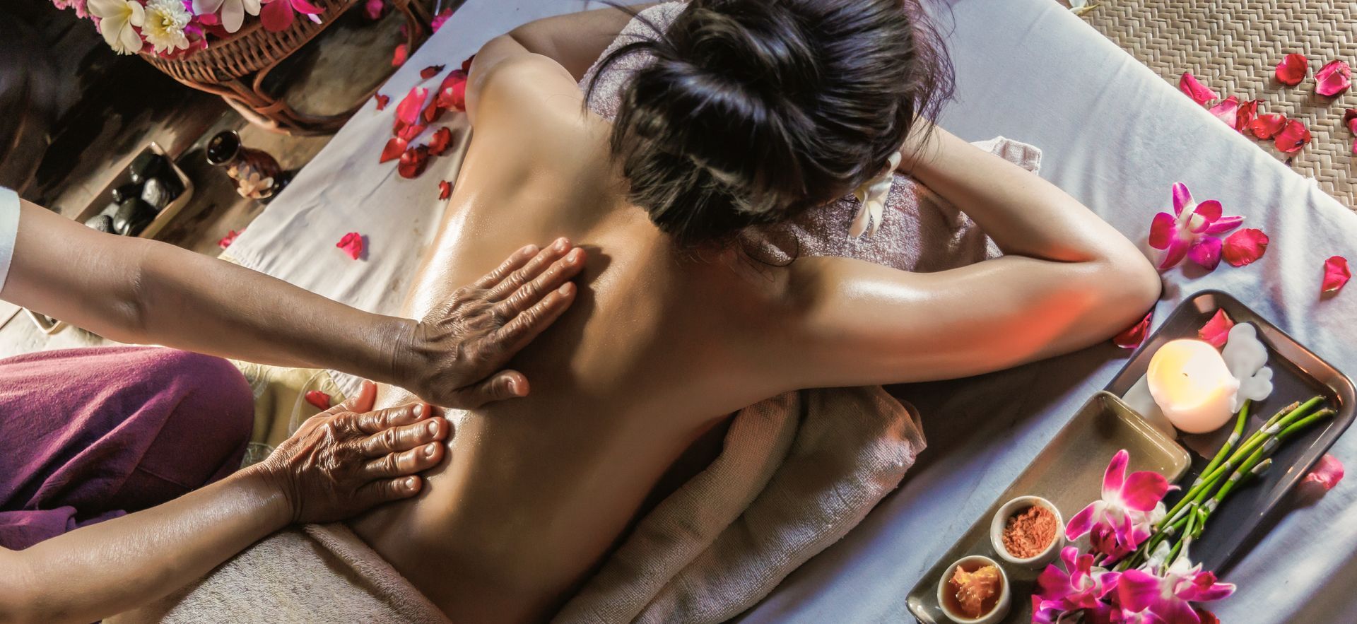 Spa massage with oils and flower petals on a person lying face down on a treatment table