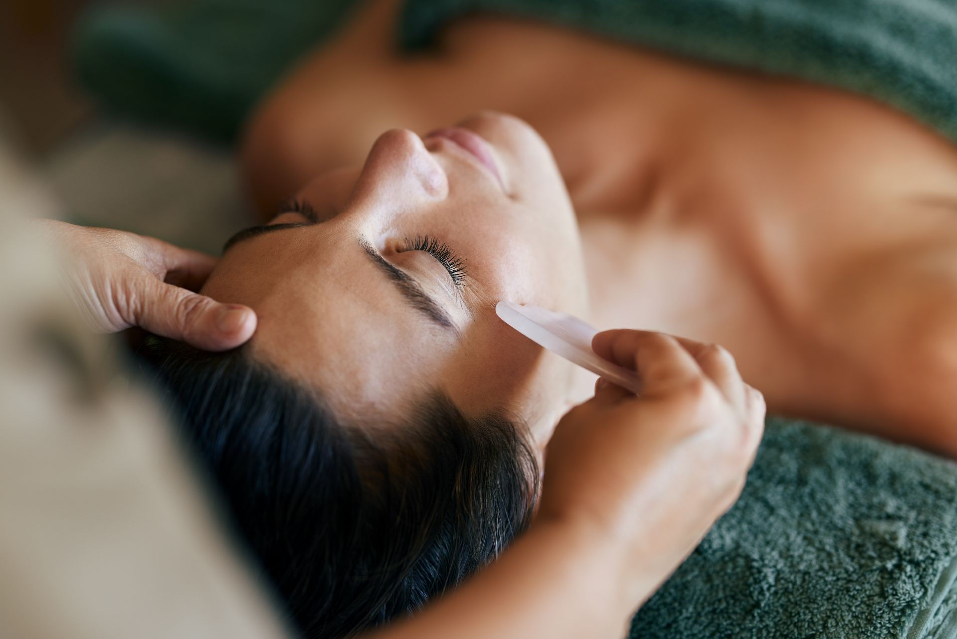Person receiving a facial massage with hands on the temples, resting on a towel-covered table
