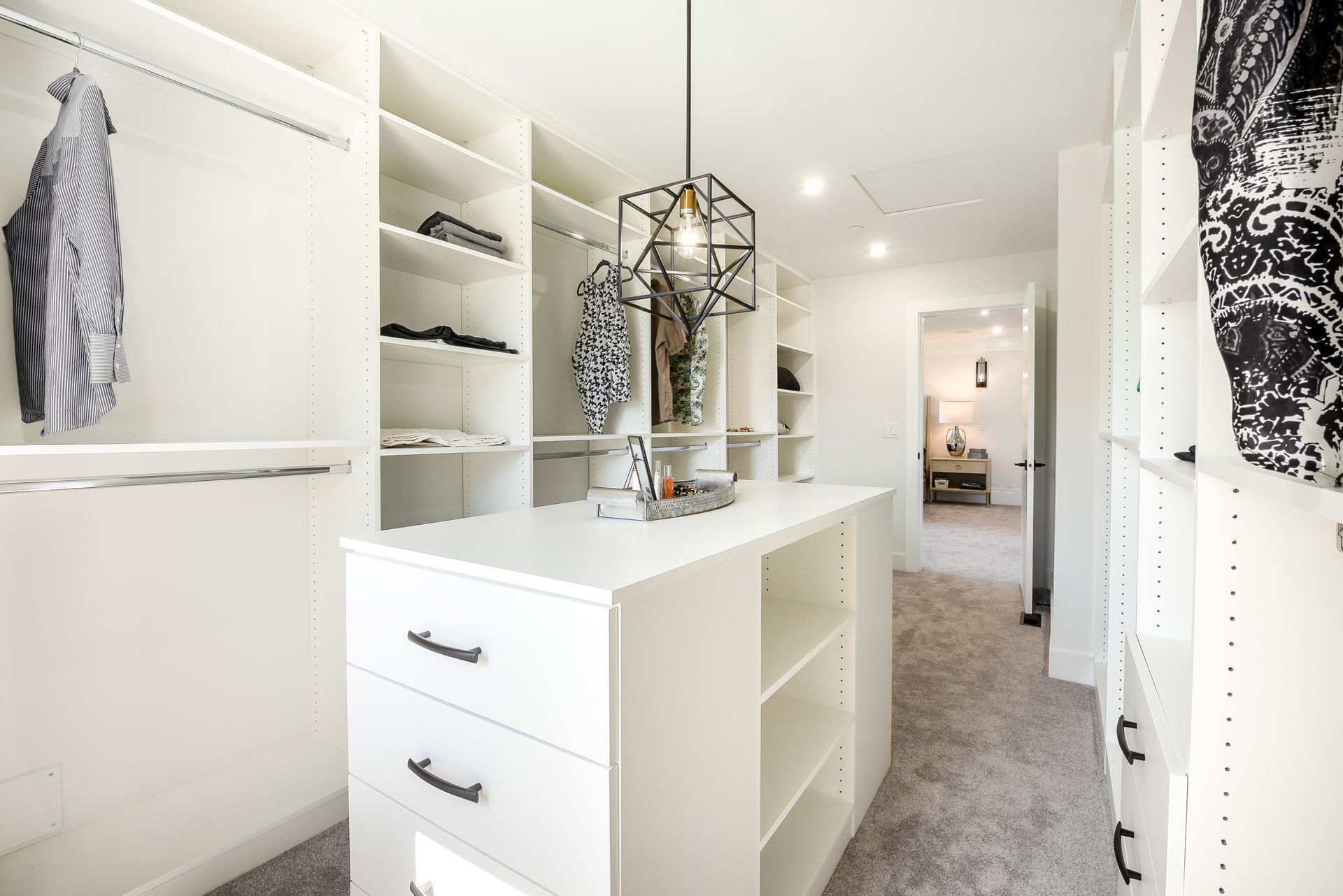 Bright white walk-in closet with built-in shelving, hanging clothes, and a central island dresser