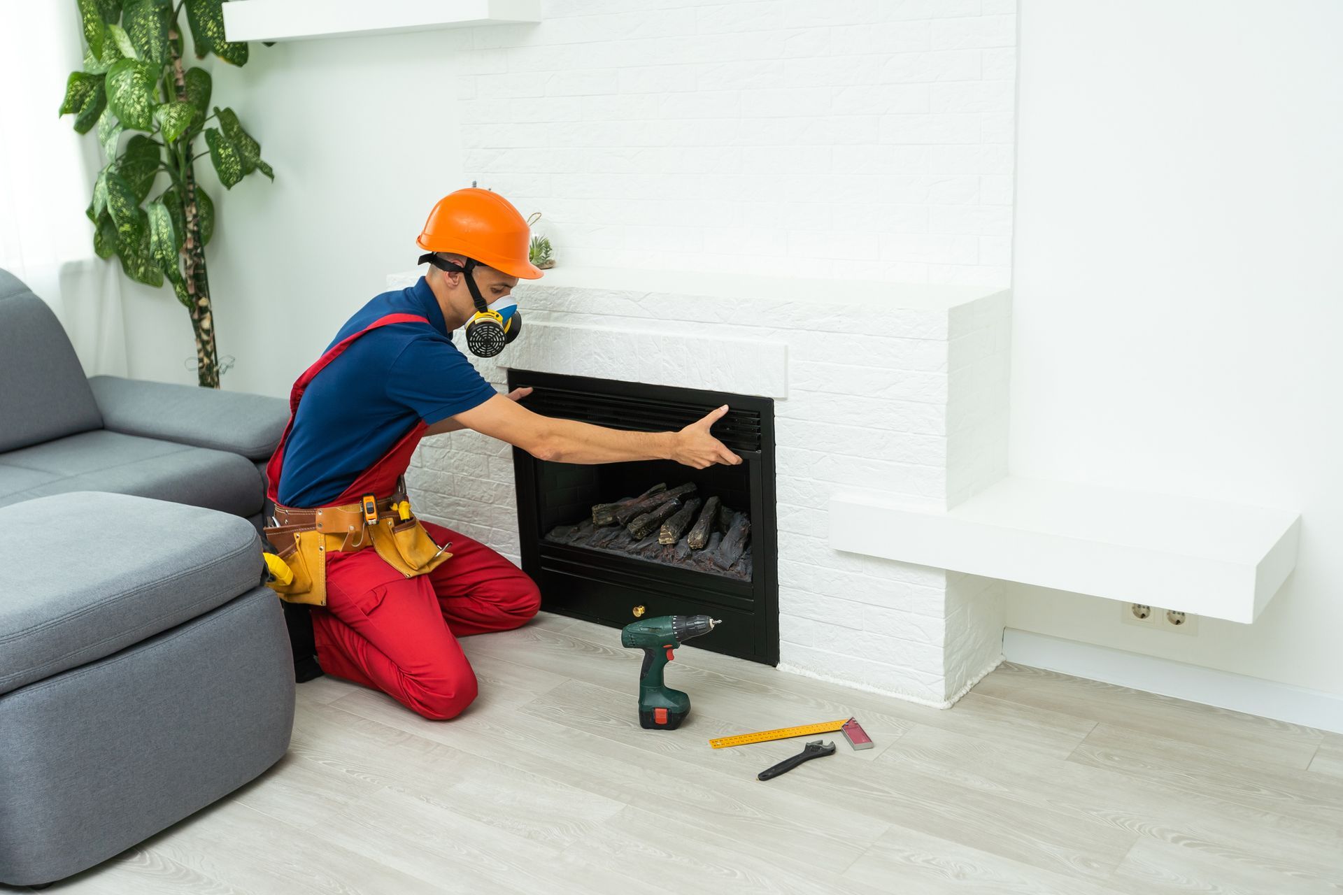 A worker in a respirator and hard hat installs a fireplace. A worker in a respirator and hard hat installs a fireplace.