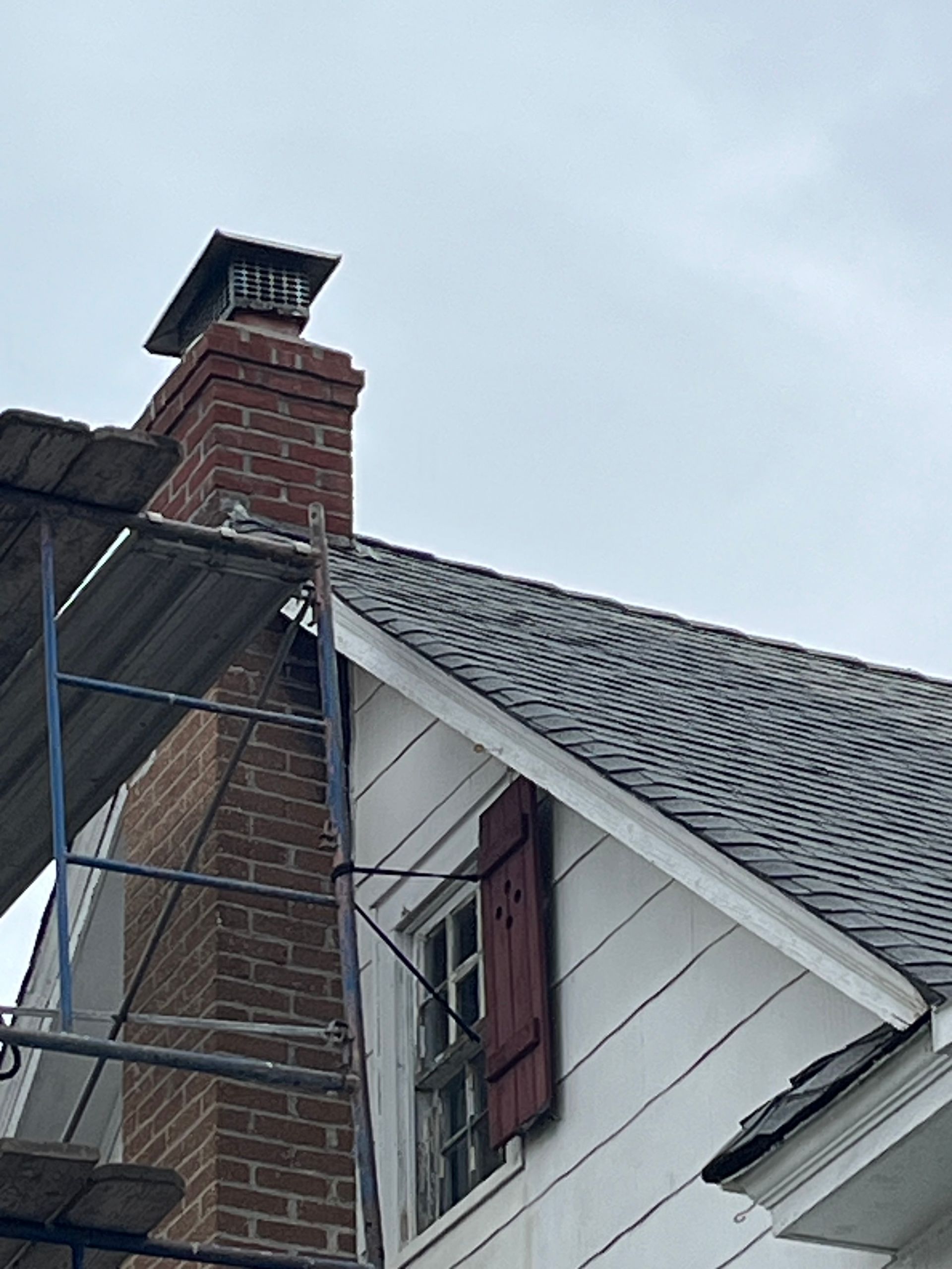 Chimney on a house with scaffolding; red brick, black roof, white siding, and cloudy sky. Chimney on a house with scaffolding; red brick, black roof, white siding, and cloudy sky.