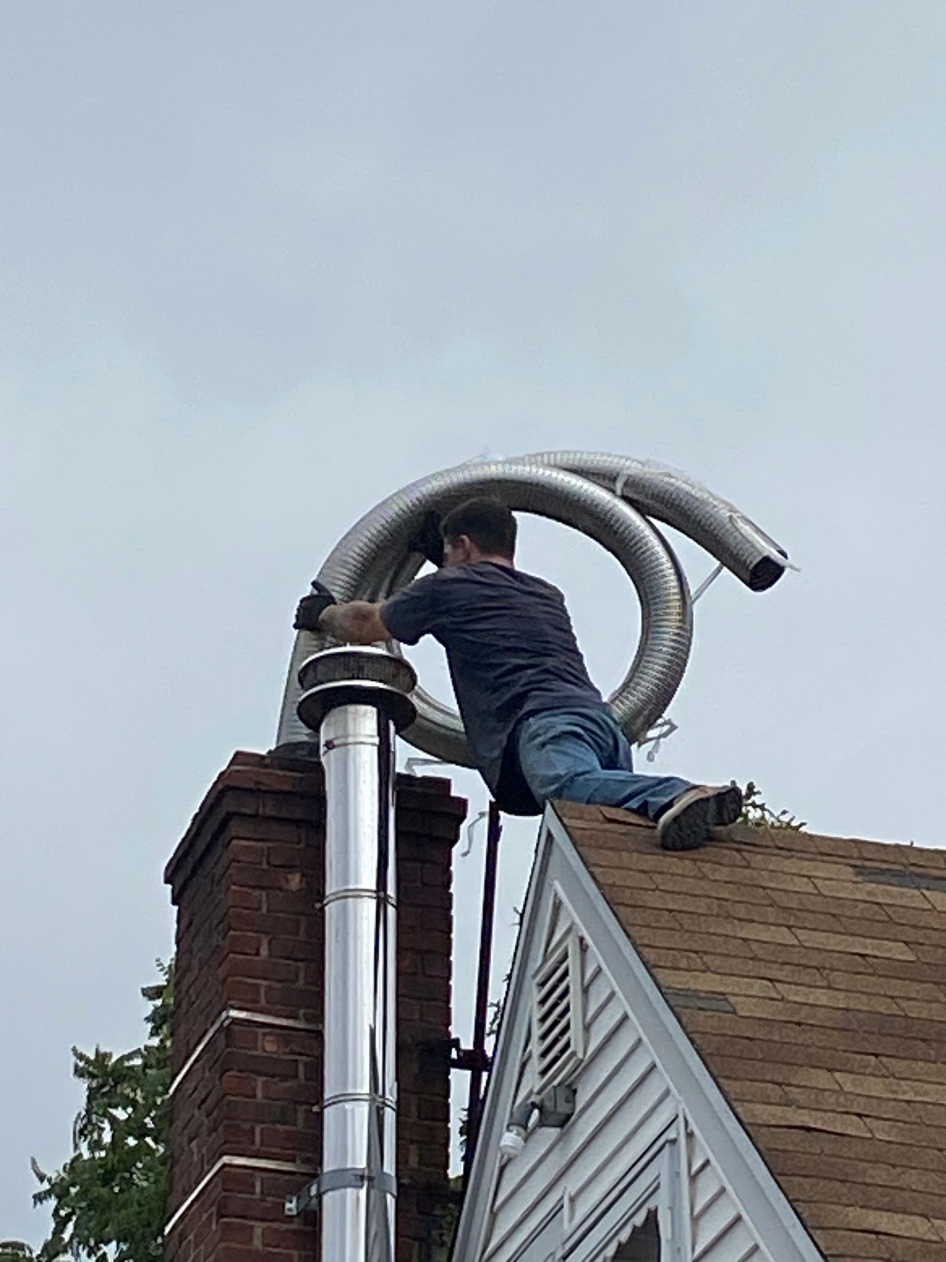 Person on a roof installing a flexible metal chimney liner. Grey sky overhead. Person on a roof installing a flexible metal chimney liner. Grey sky overhead.