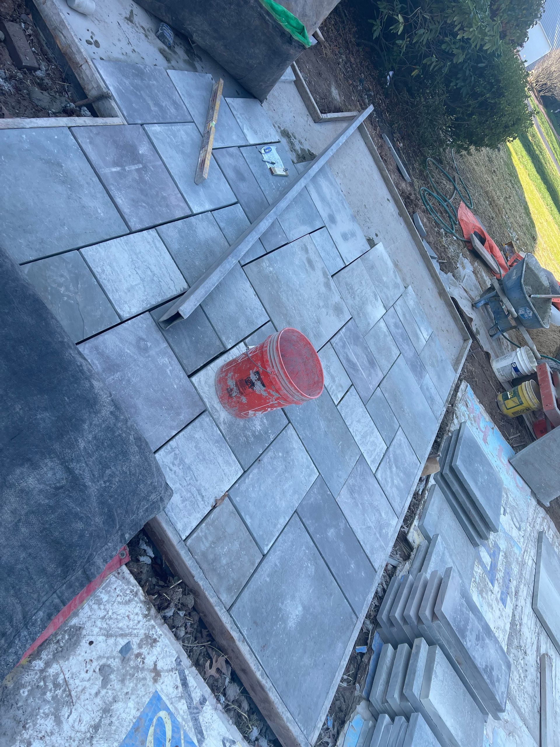 A concrete walkway is being built with a red bucket on the ground.