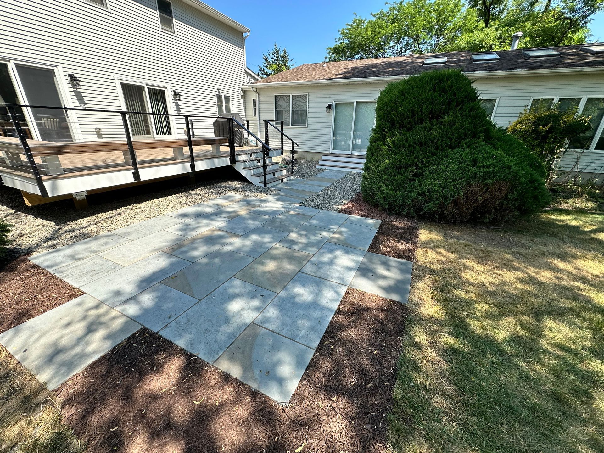A patio with a deck and stairs in front of a house.