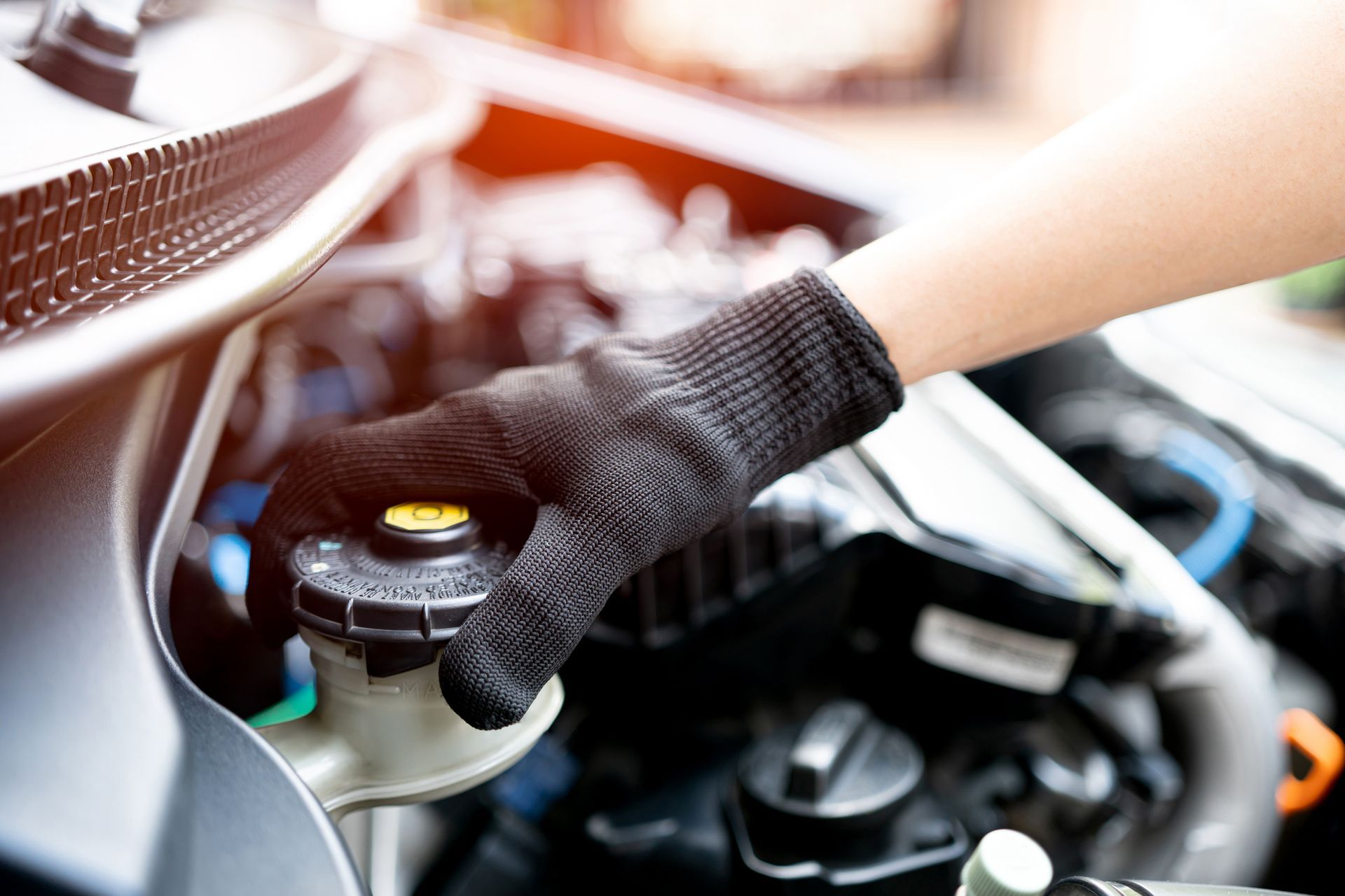Gloved hand checking brake fluid reservoir in a car engine bay.