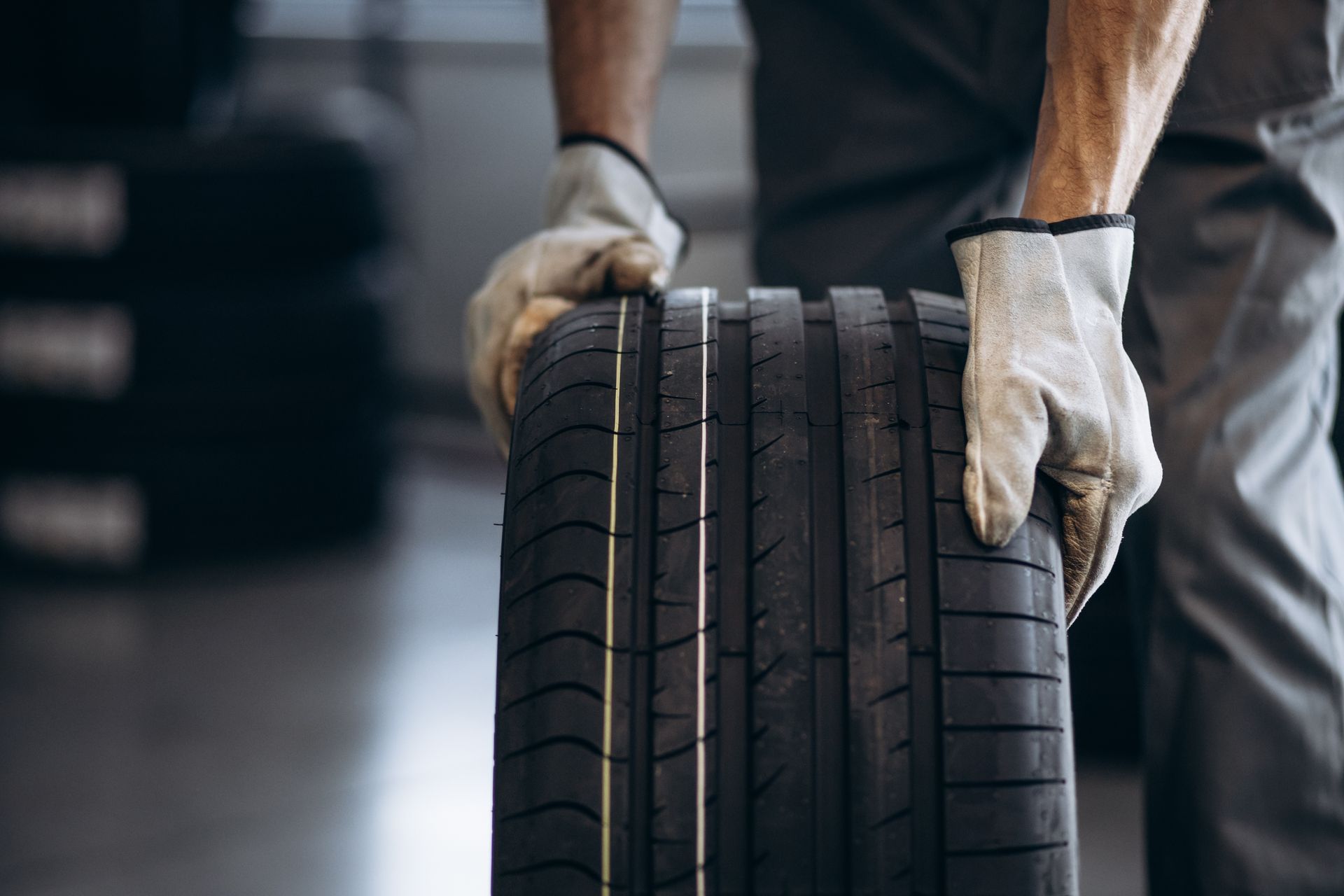 Mechanic holding a new car tire with gloved hands in a garage setting.