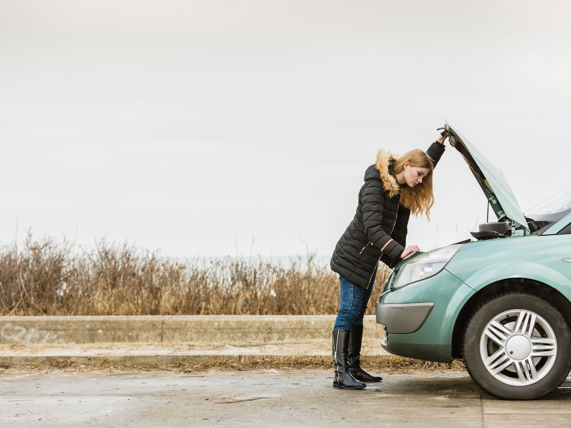 Woman inspecting a teal car with the hood open on a roadside