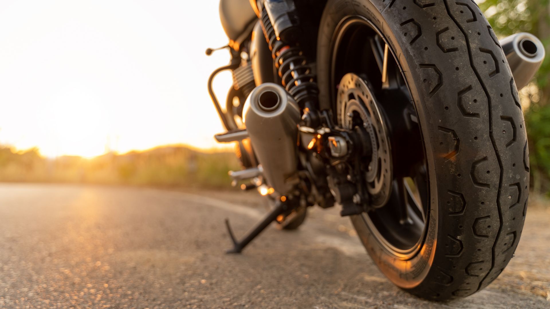Close-up of a motorcycle rear wheel and exhaust on a sunlit road at sunset Close-up of a motorcycle rear wheel and exhaust on a sunlit road at sunset