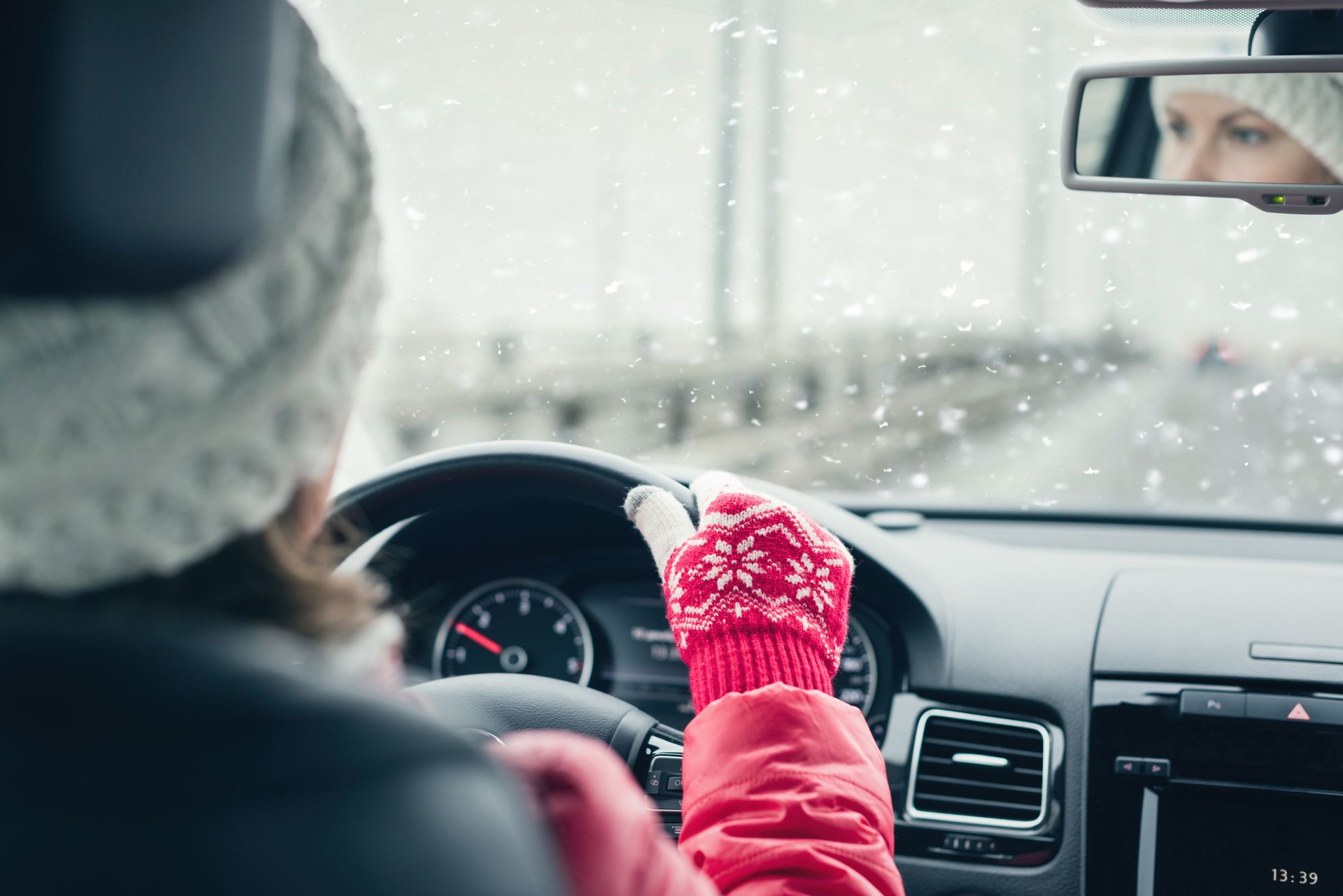 Woman driving car in snowy weather, wearing red mitten and hat.