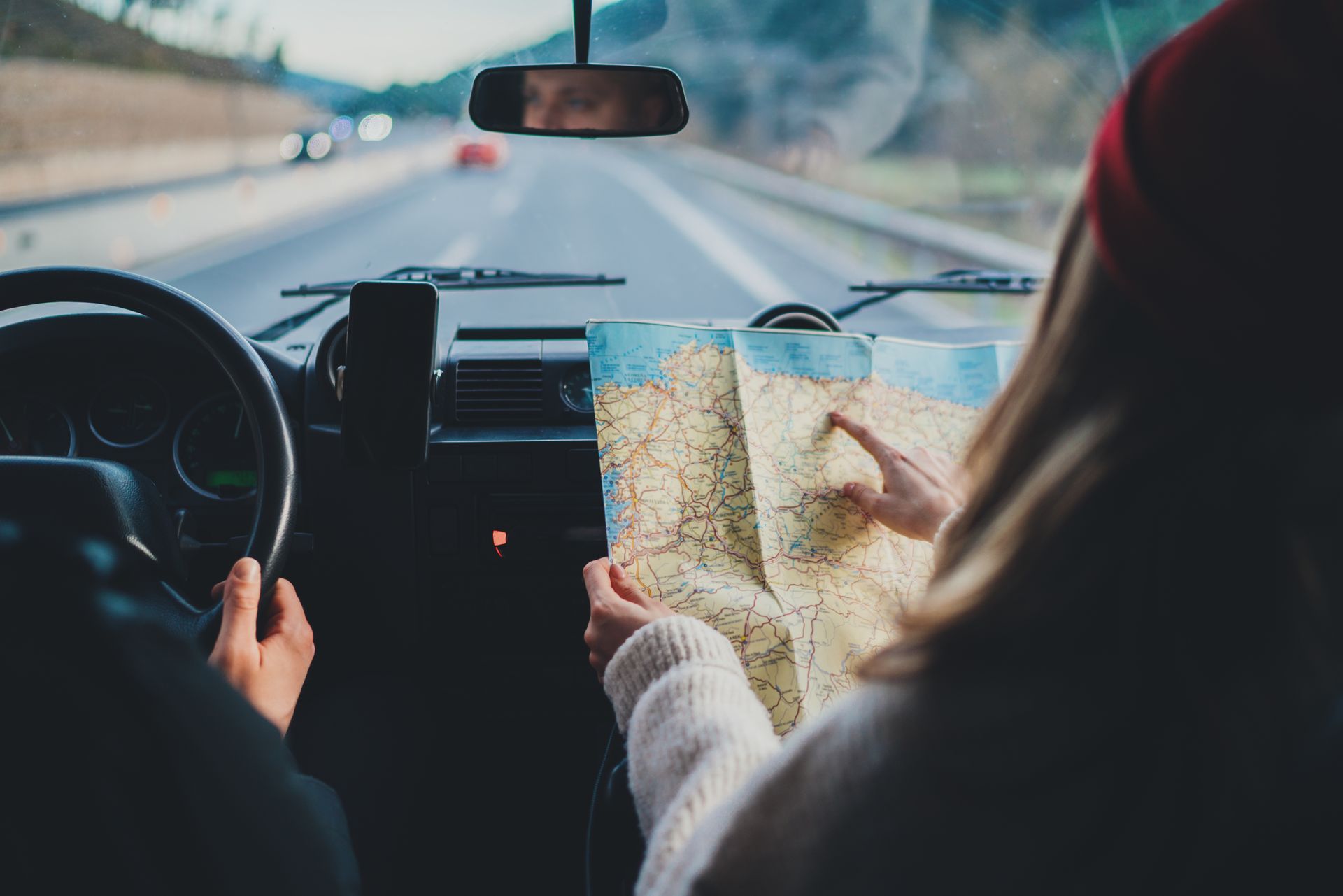 Two people in a car navigating with a paper map on a road trip