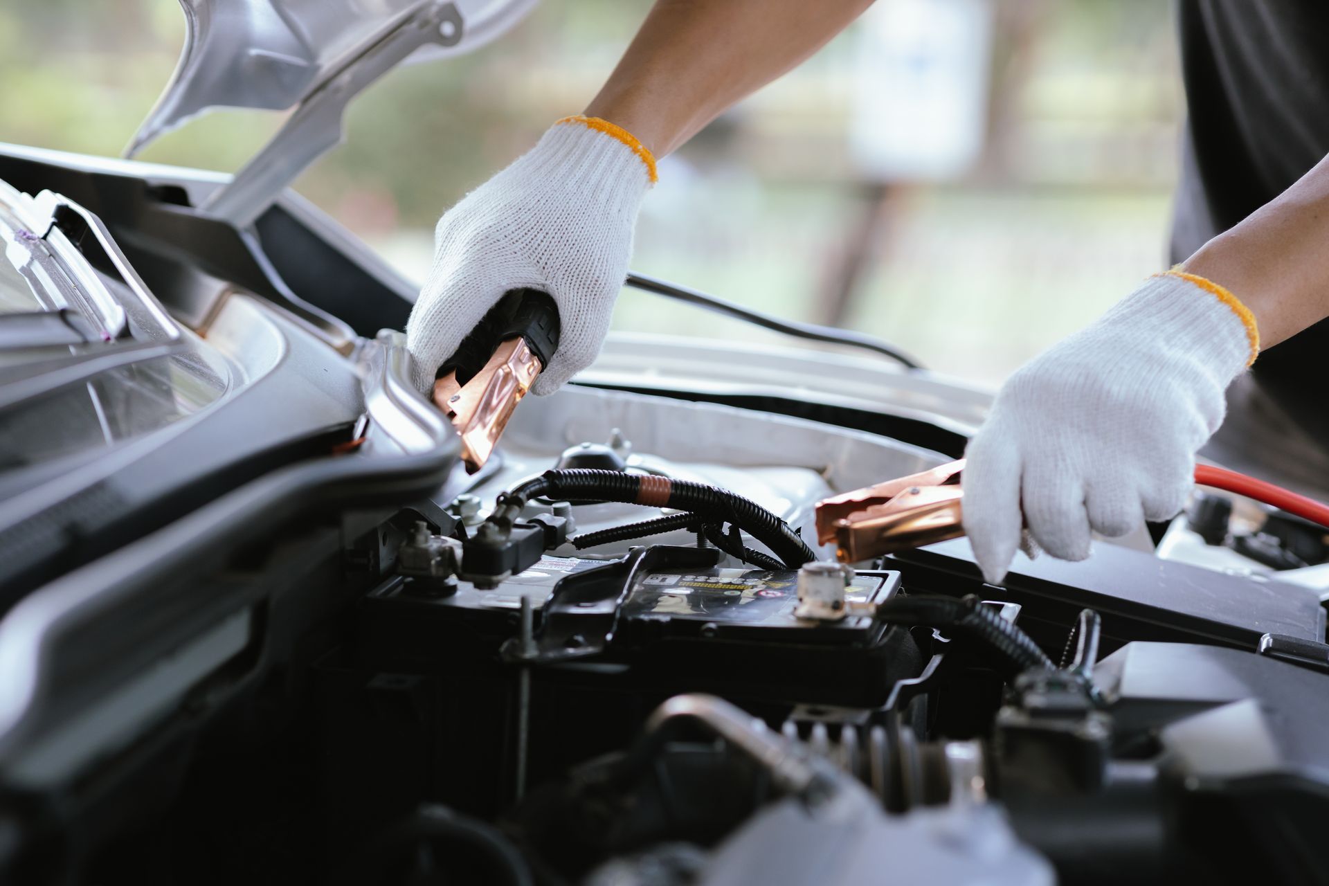 Hands in white gloves connecting jumper cables to a car battery under the open hood. Hands in white gloves connecting jumper cables to a car battery under the open hood.