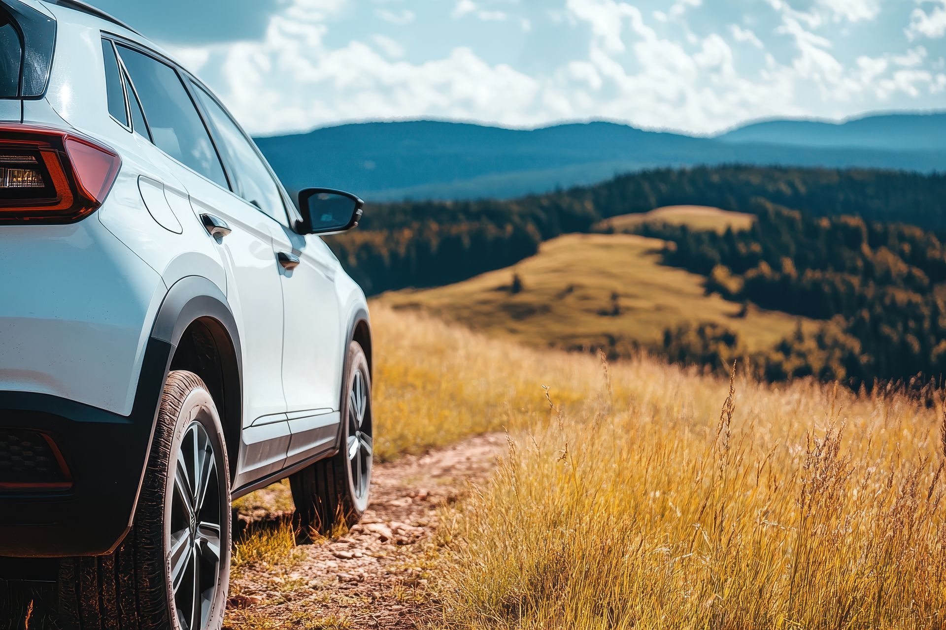 White SUV parked on a grassy hill with mountains in the background