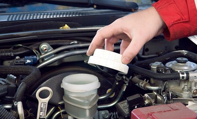 A person is pouring brake fluid into a container under the hood of a car A person is pouring brake fluid into a container under the hood of a car