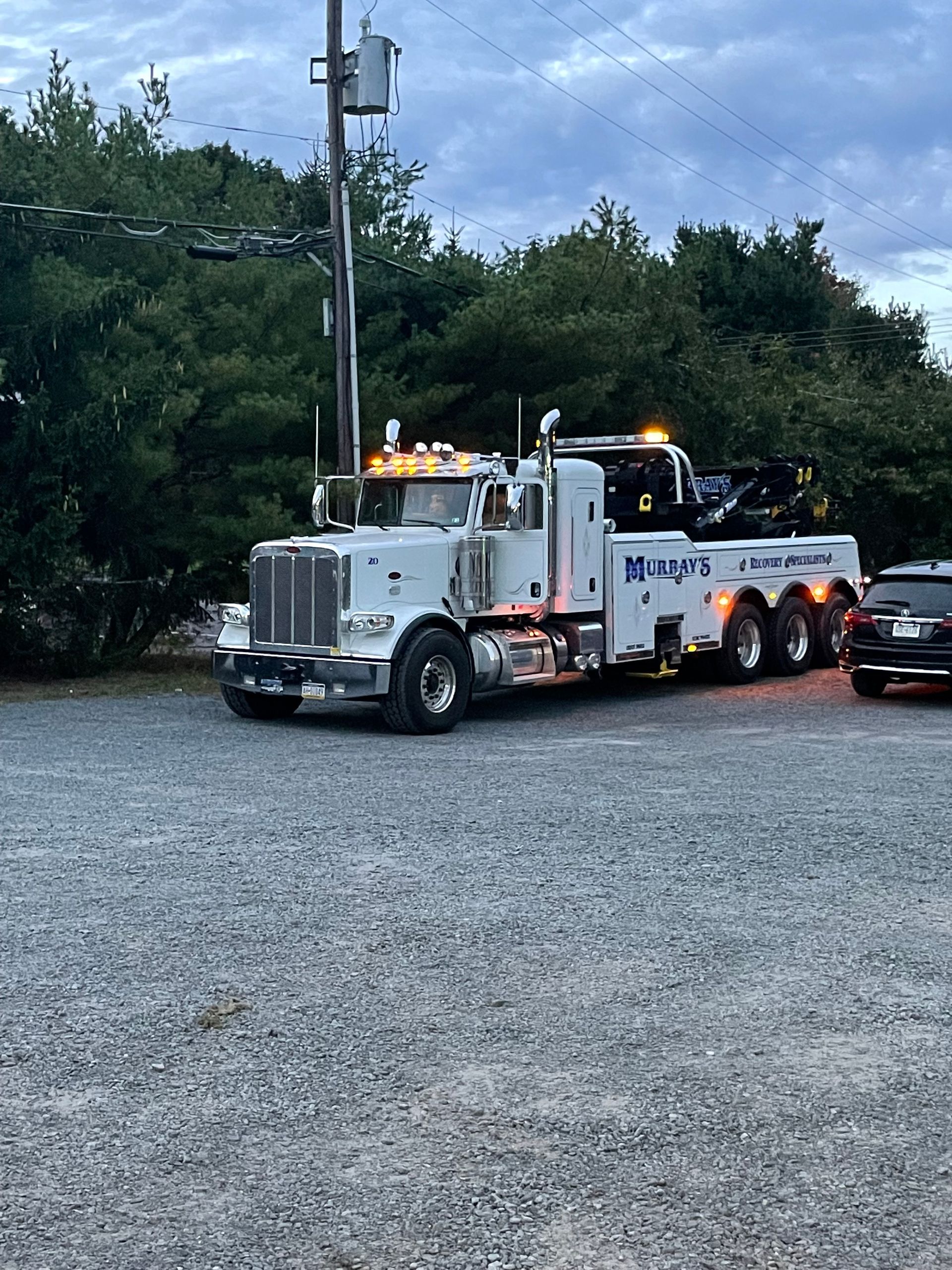 A tow truck is parked in a gravel lot next to a car.