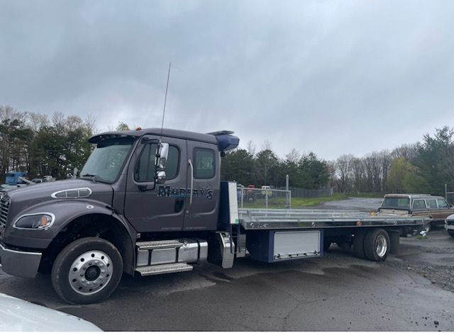 A flatbed tow truck is parked in a parking lot.