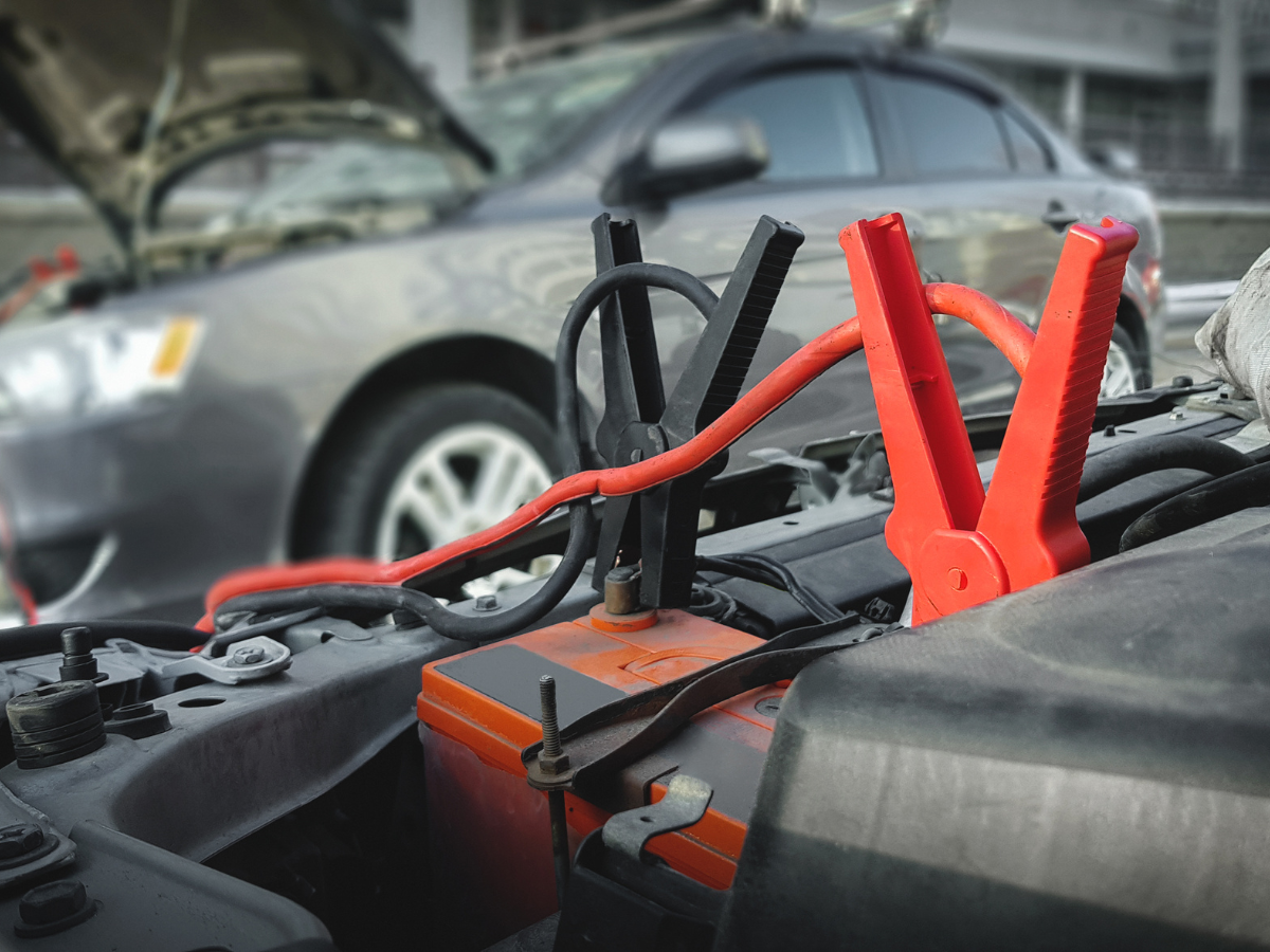 Jumper cables connecting two car batteries, with the hood of a gray car open. Jumper cables connecting two car batteries, with the hood of a gray car open.