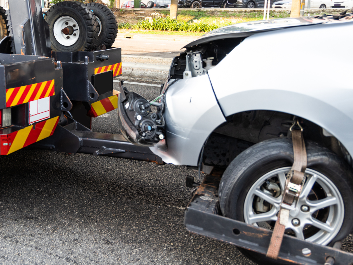 Silver car damaged in a collision being towed by a tow truck.