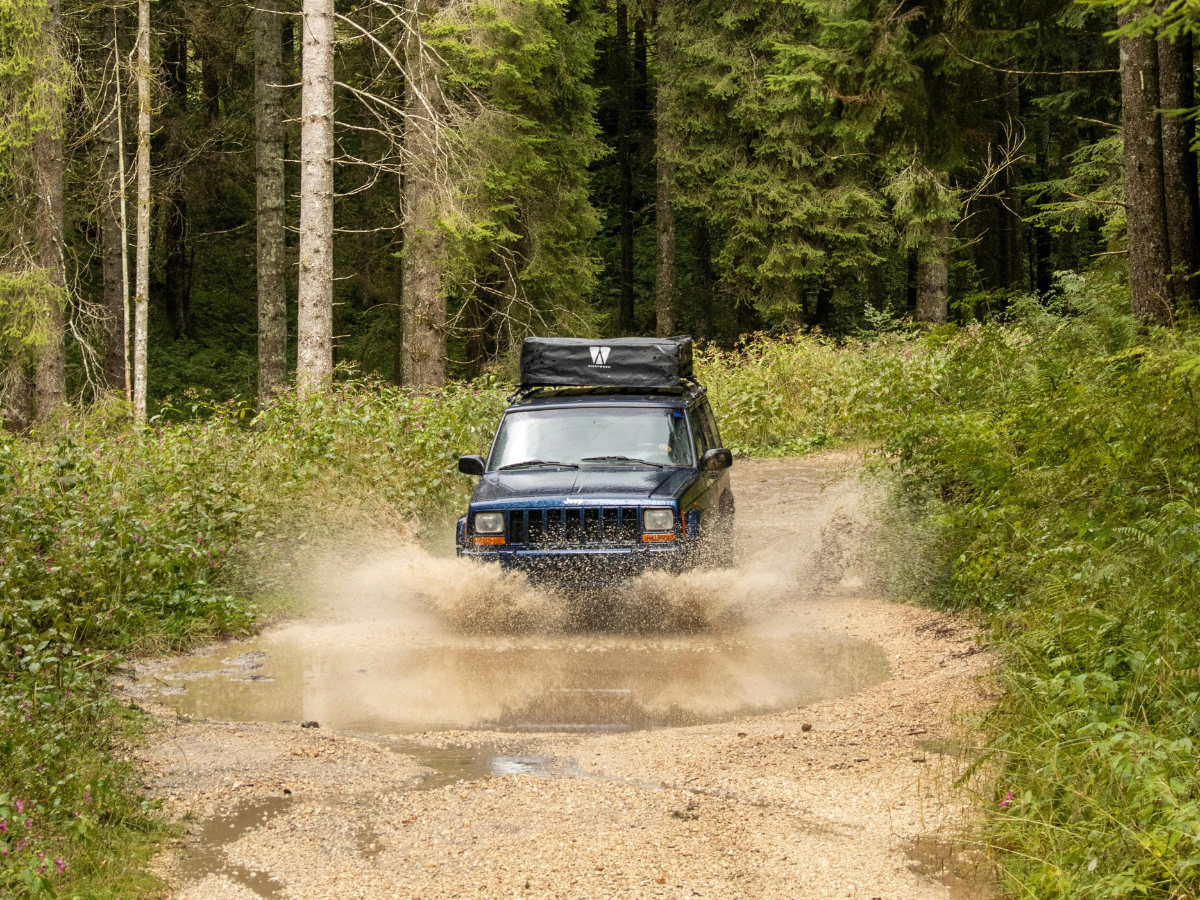 Blue SUV splashes through a muddy puddle on a forest trail, trees in the background. Blue SUV splashes through a muddy puddle on a forest trail, trees in the background.